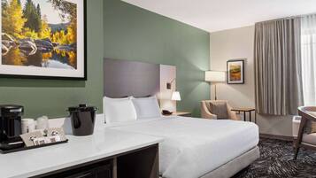 A hotel room with a bed, a desk with a coffee maker, a lamp, and a painting on the wall.