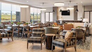 Een ruime hotellobby met moderne meubels, grote ramen met uitzicht op de omgeving en een wandgemonteerde flatscreen televisie.