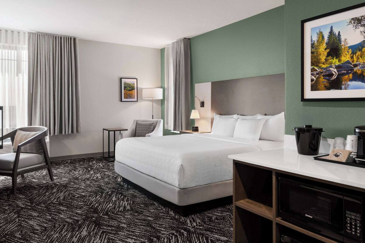 Une chambre d’hôtel avec un grand lit, un bureau avec une machine à café, une chaise, une lampe et un tableau encadré au mur.