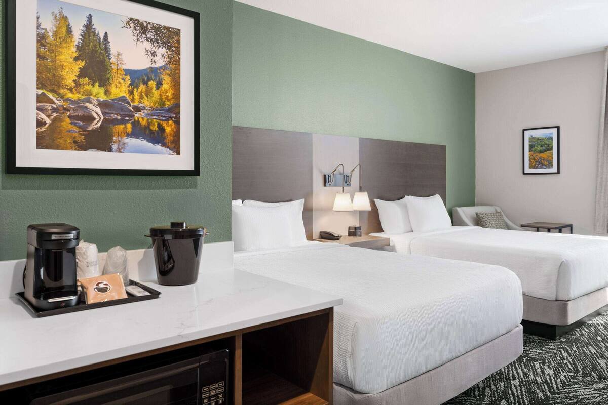 Une chambre d’hôtel avec deux lits, un bureau doté d’une machine à café, une lampe et un tableau représentant un paysage.