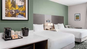 Ein Hotelzimmer mit zwei Betten, einem Schreibtisch mit Kaffeemaschine, einer Lampe und einem Landschaftsbild.