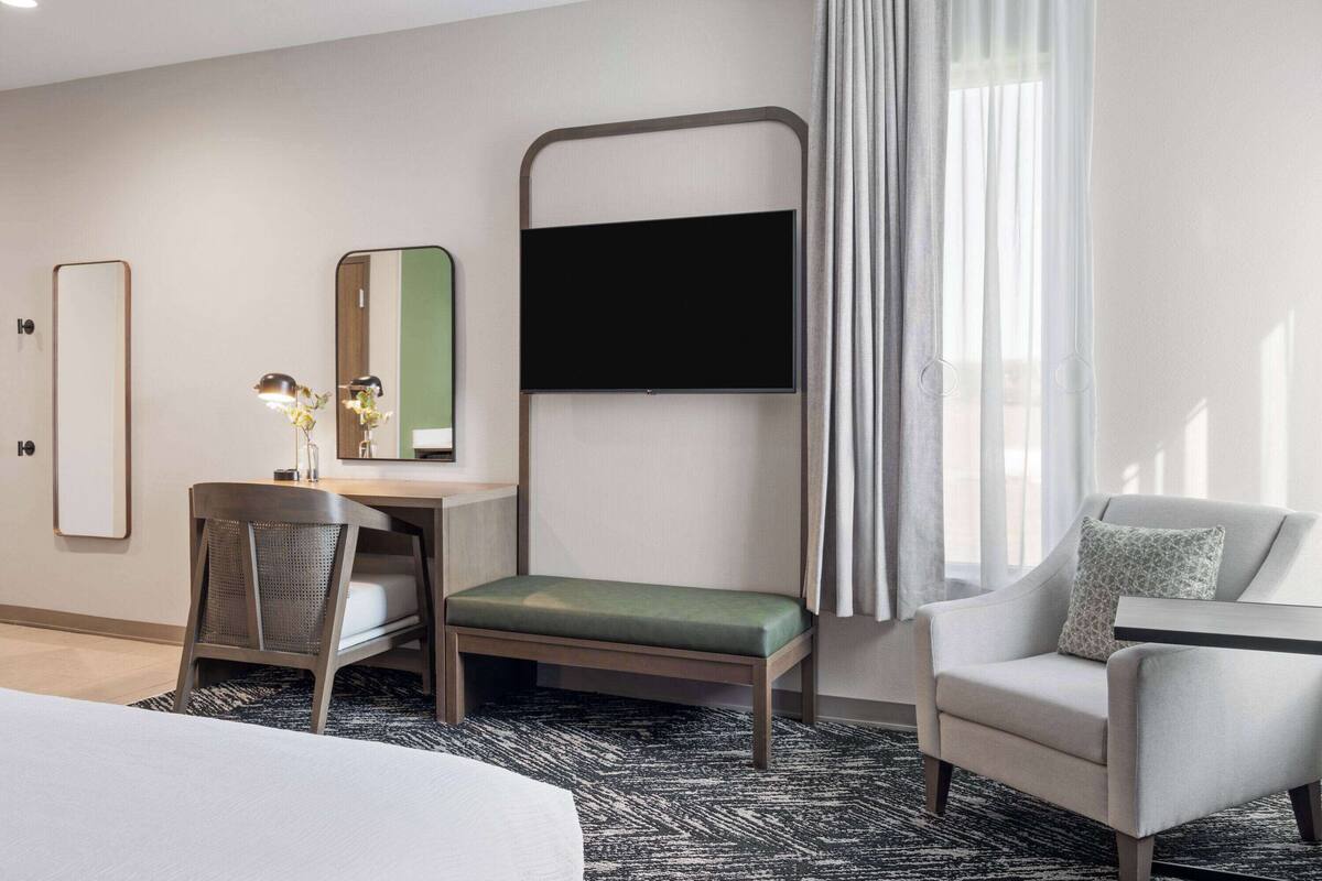 Une chambre d’hôtel comprenant un lit, un bureau avec une chaise, un canapé, une télévision et une fenêtre avec des rideaux.