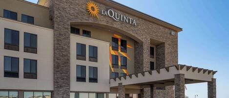 Hotel La Quinta con fachada de piedra, ventanas amplias y una zona de entrada cubierta.