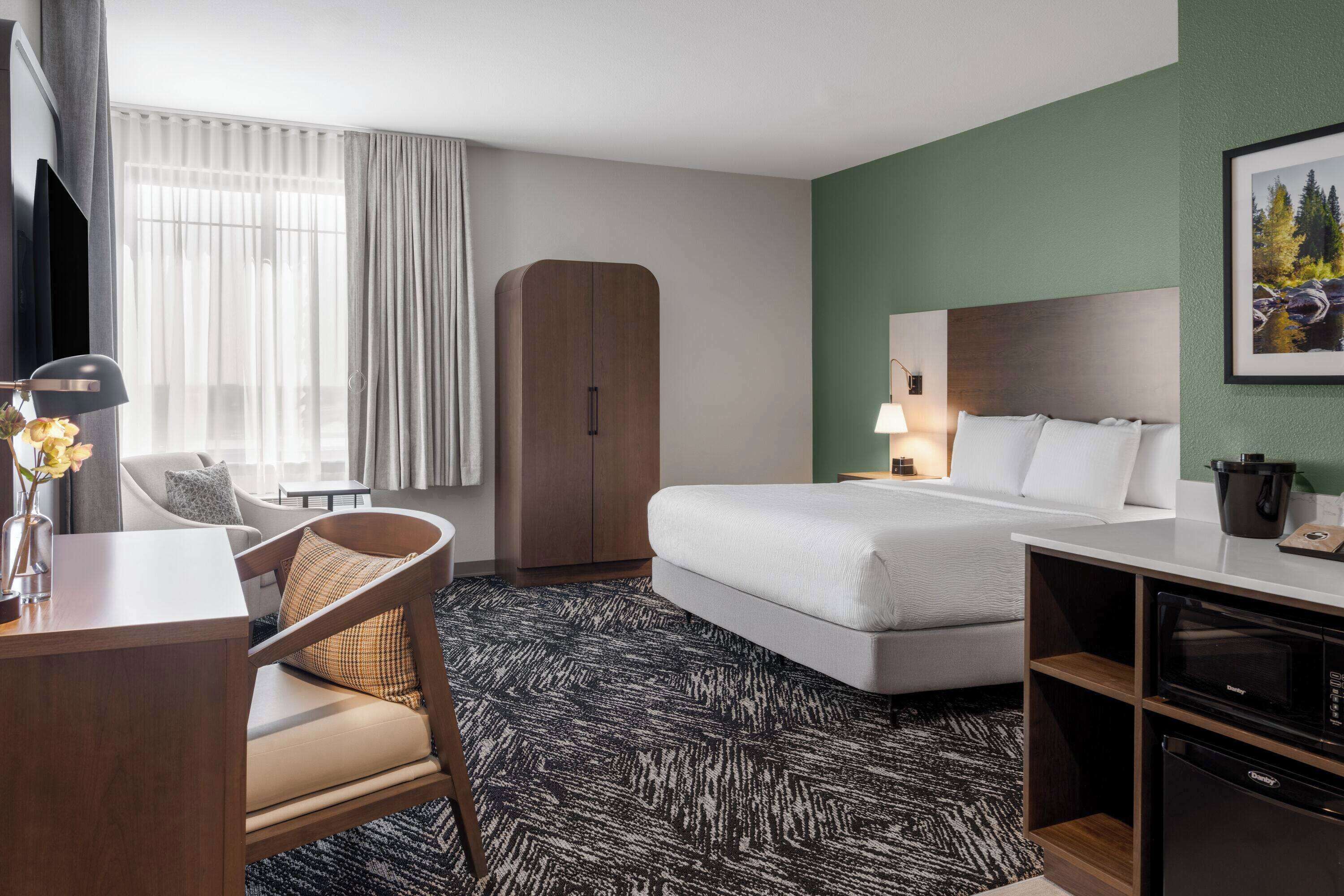 Habitación de hotel con cama, escritorio, silla, armario, televisor y microondas.