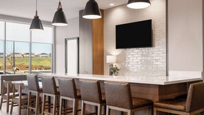 Een moderne keuken met een groot eiland, barstoelen, hanglampen en een flatscreen-tv aan de muur.