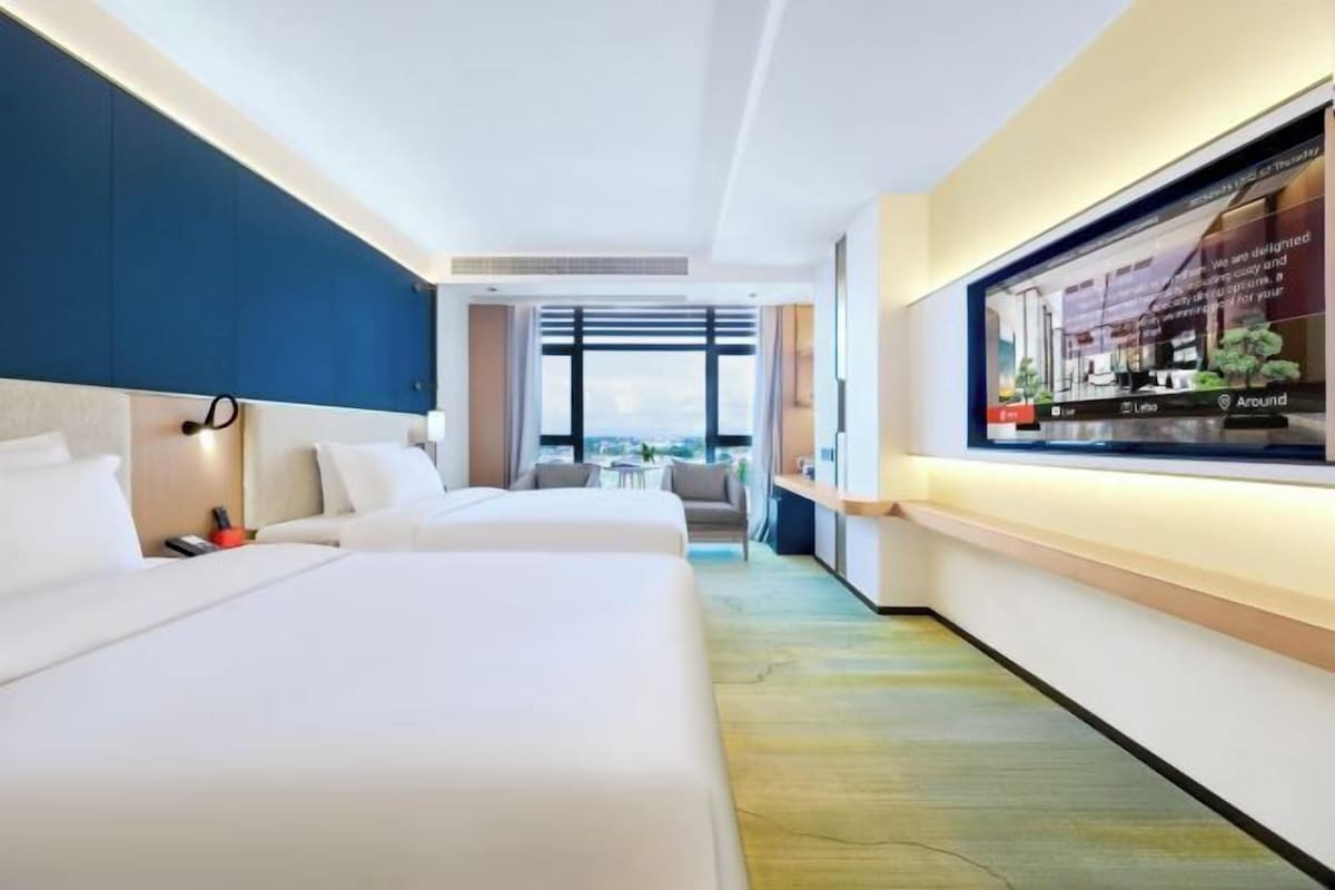 A hotel room with two beds, a TV, and a view of the city.