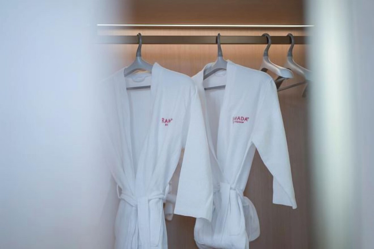 Two white robes hanging on a rack in a room with a wooden wall and a horizontal light fixture above.