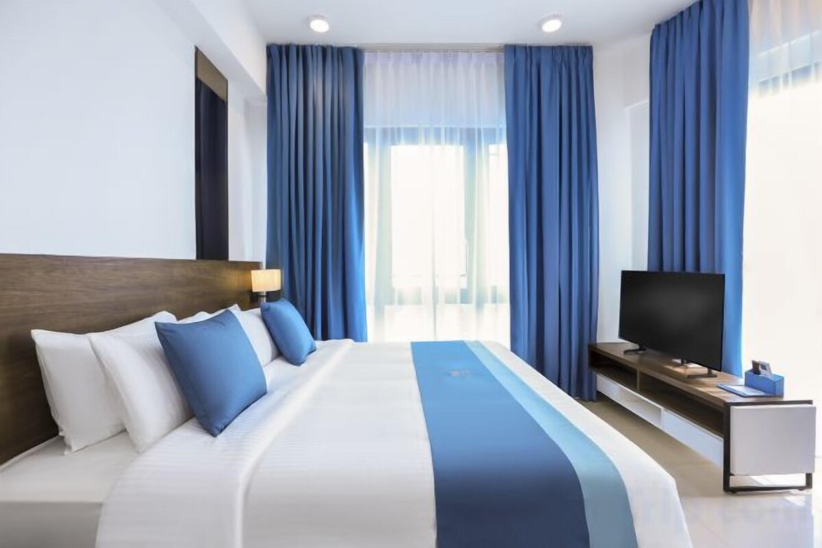 A hotel room with a large bed, a flat-screen TV, and a desk with a lamp.