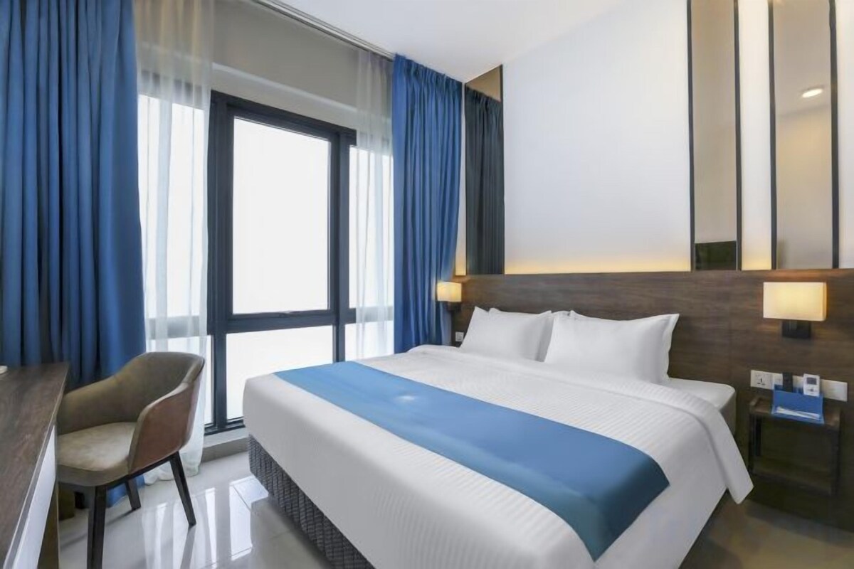 A hotel room with a large bed, a desk, and a chair.