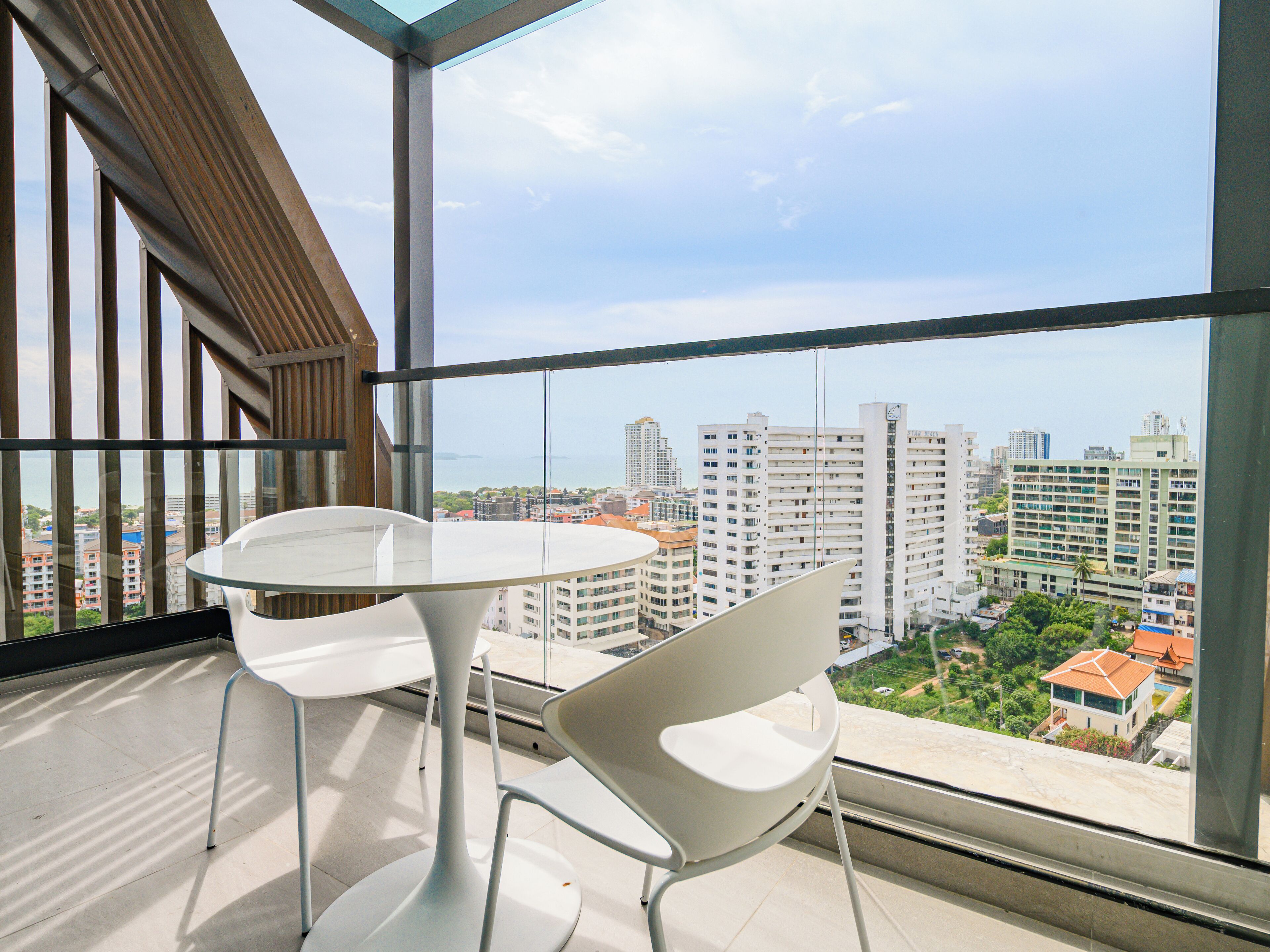 A balcony with a glass partition, two white chairs, and a round table.