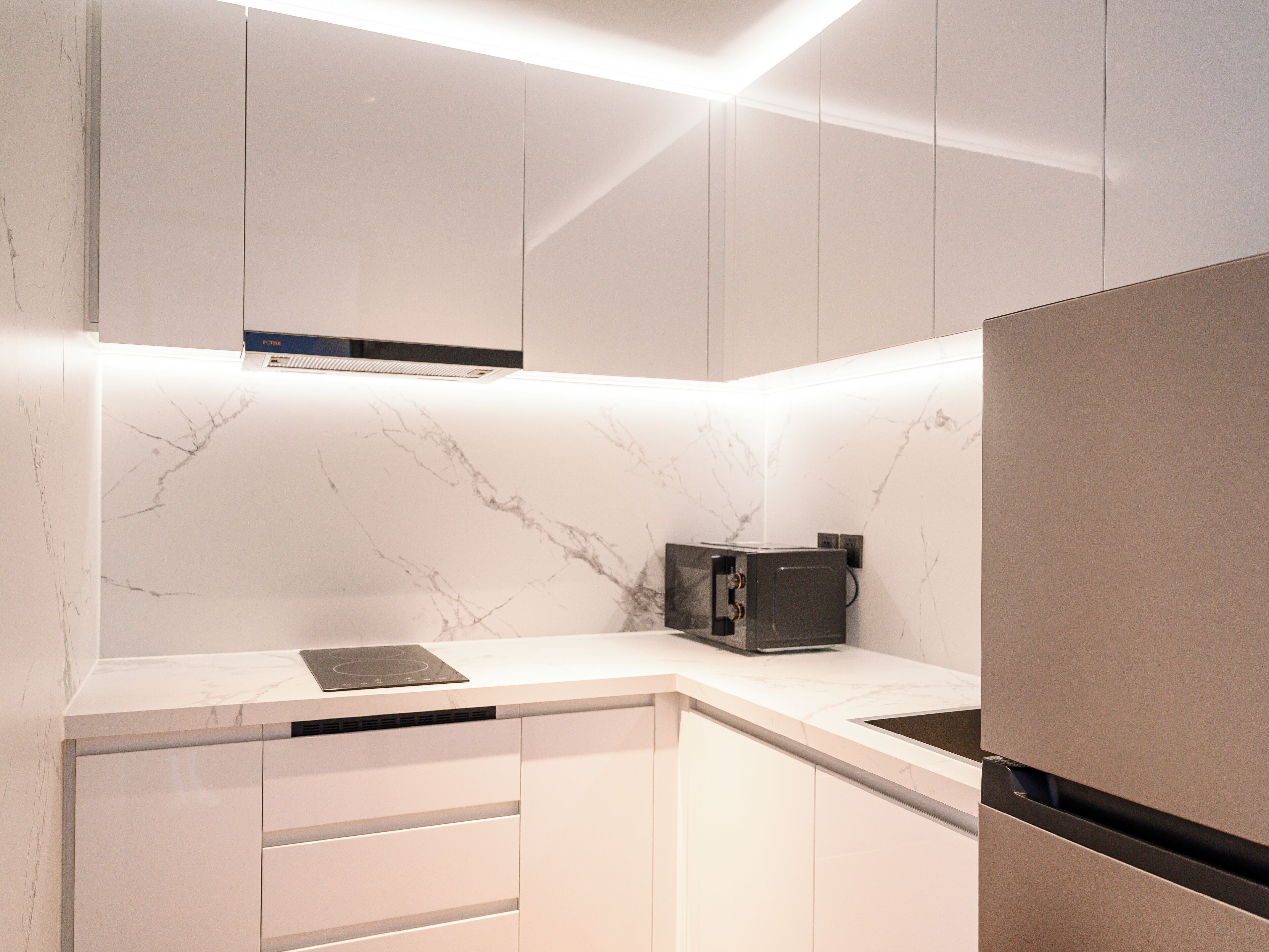 A modern kitchen with white cabinetry, a marble backsplash, and built-in appliances.
