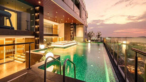 Un hotel moderno con piscina a sfioro sul tetto, ringhiera in vetro e vista sulla città al tramonto.