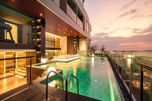 A modern hotel with a rooftop infinity pool, a glass balustrade, and a city view at sunset. - Beverly Mountain Bay, Trademark Collection By Wyndham (Pattaya)