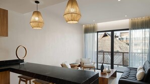 A modern kitchen with a black island and wooden stools, a dining area with a sofa and chairs, and large windows with a view of a building. - Wyndham Residences Tulum (Tulum)