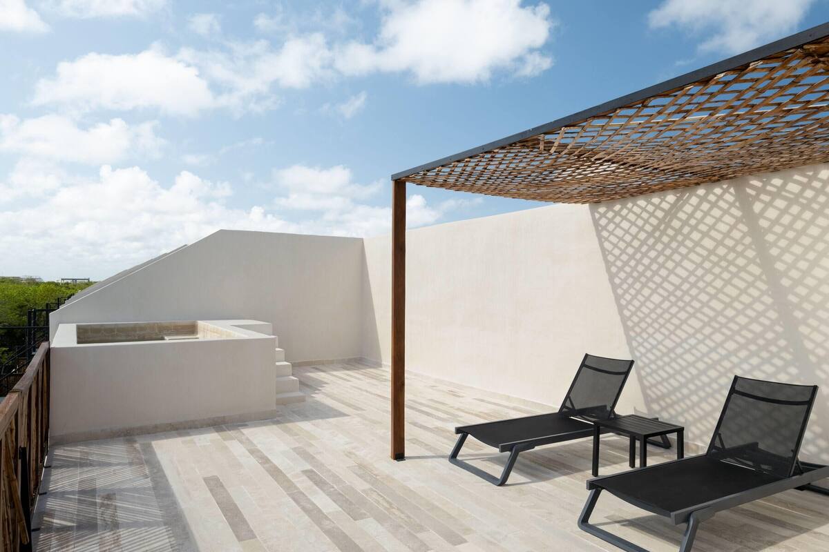 A rooftop terrace with a pergola, two lounge chairs, and a small seating area.