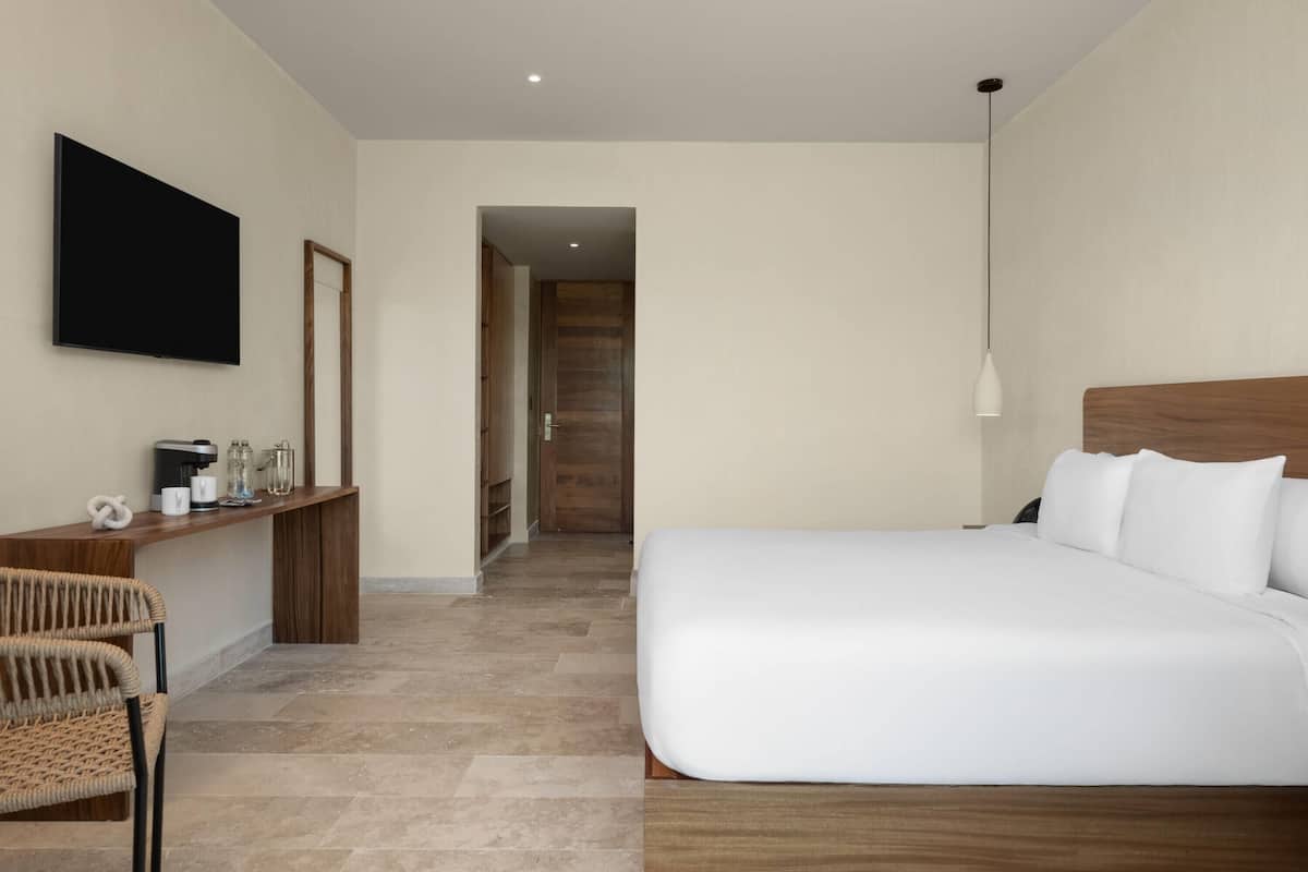 A modern hotel room with a large bed, a desk with a flat-screen TV, and a wooden headboard.
