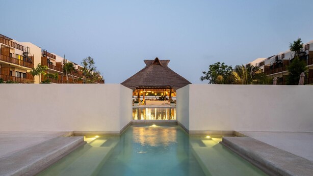 A swimming pool with a bar area in the center, surrounded by buildings with balconies. - Wyndham Residences Tulum (Tulum)