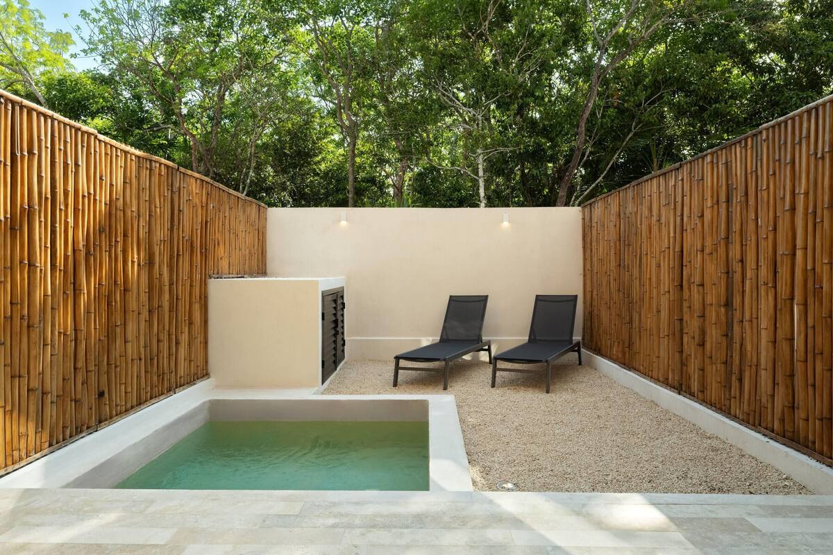 A private outdoor area with a hot tub, two lounge chairs, and a wooden fence.