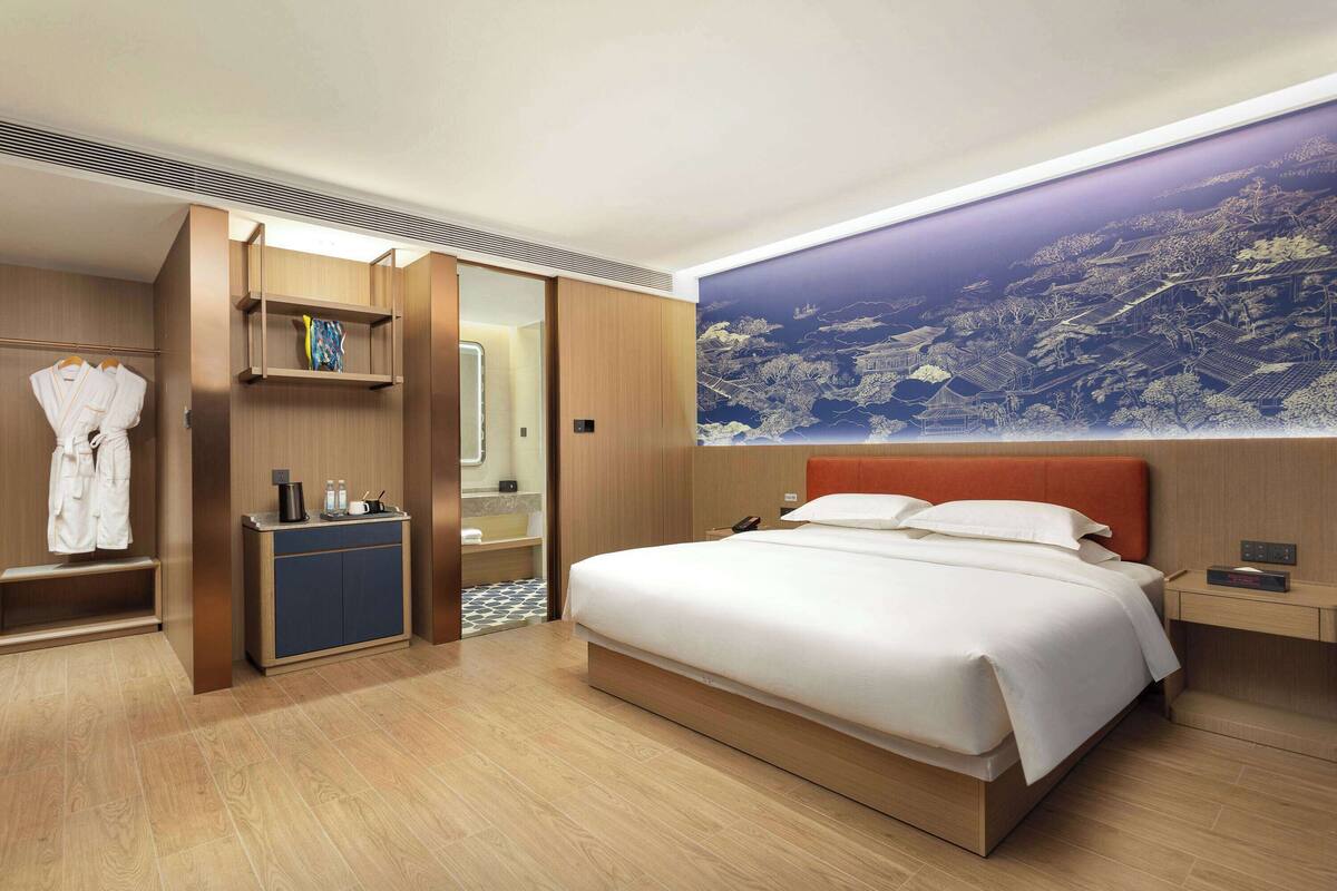 Ein Hotelzimmer mit einem großen Bett, einem Kleiderschrank, einem Frisiertisch und einem Wandgemälde.