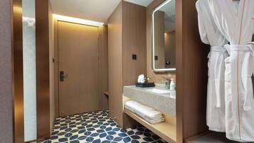 A hotel bathroom with a wooden vanity, a large mirror, a robe hanging on the wall, and a patterned floor.