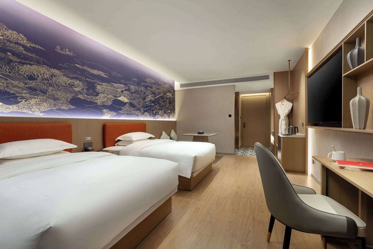 Ein Hotelzimmer mit zwei Betten, einem Schreibtisch, einem Fernseher und einem großen Wandbild.