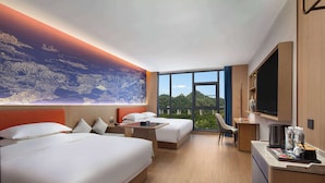 A hotel room with two beds, a desk, a chair, a TV, and a large window with a view of greenery. - Hawthorn By Wyndham Fenghuang Baiyue (Xiangxi)