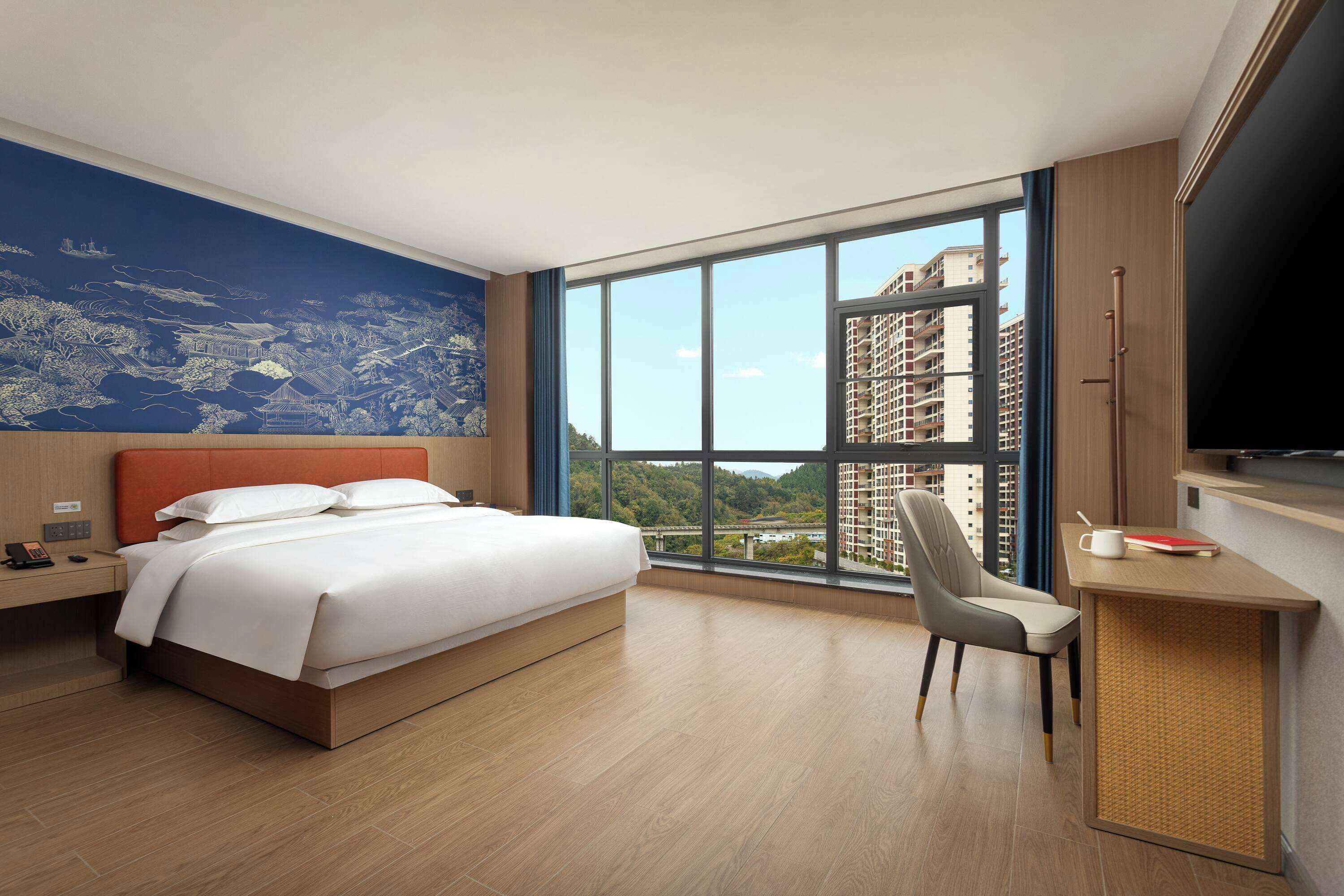 Una habitación de hotel moderna con una cama grande, un escritorio, una silla y un televisor.