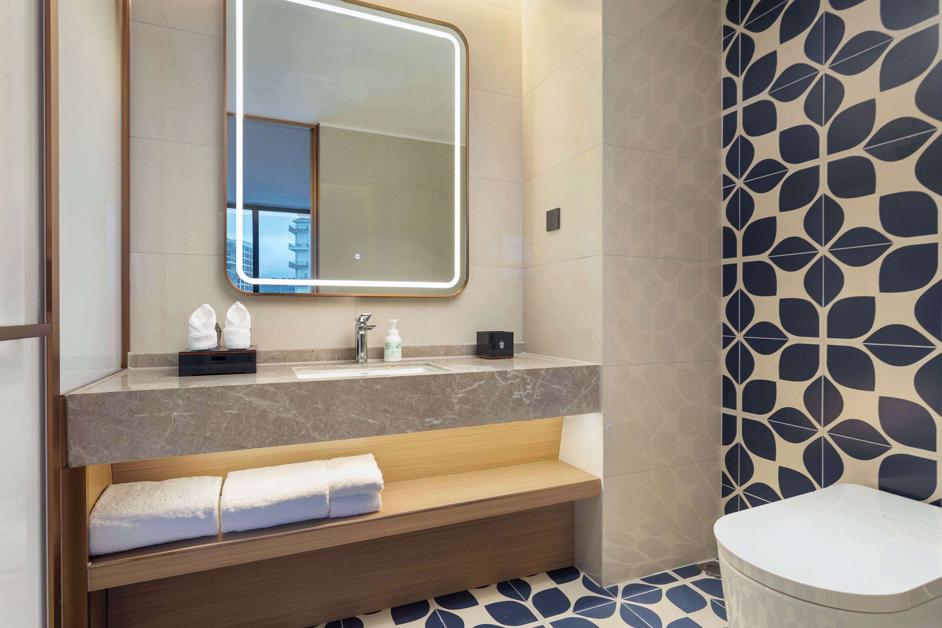 A modern bathroom with a marble sink, a large mirror, and a patterned wall.