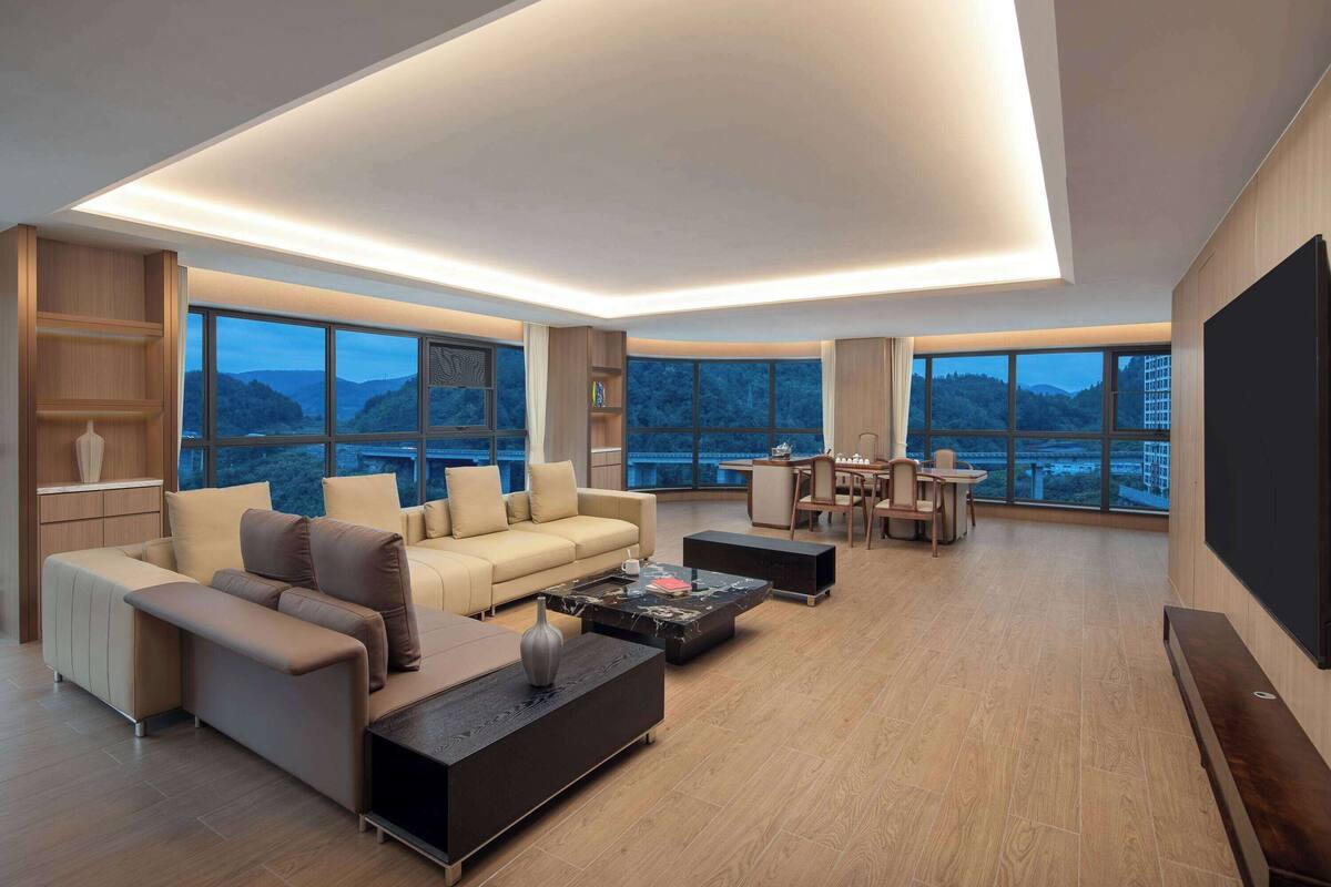 Ein modernes Wohnzimmer mit Sofa, Couchtisch und Fernseher. Große Fenster bieten Blick auf die Berge.