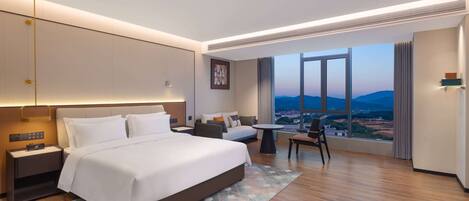 A modern hotel room with a large bed, a desk, a sofa, and a view of the cityscape.