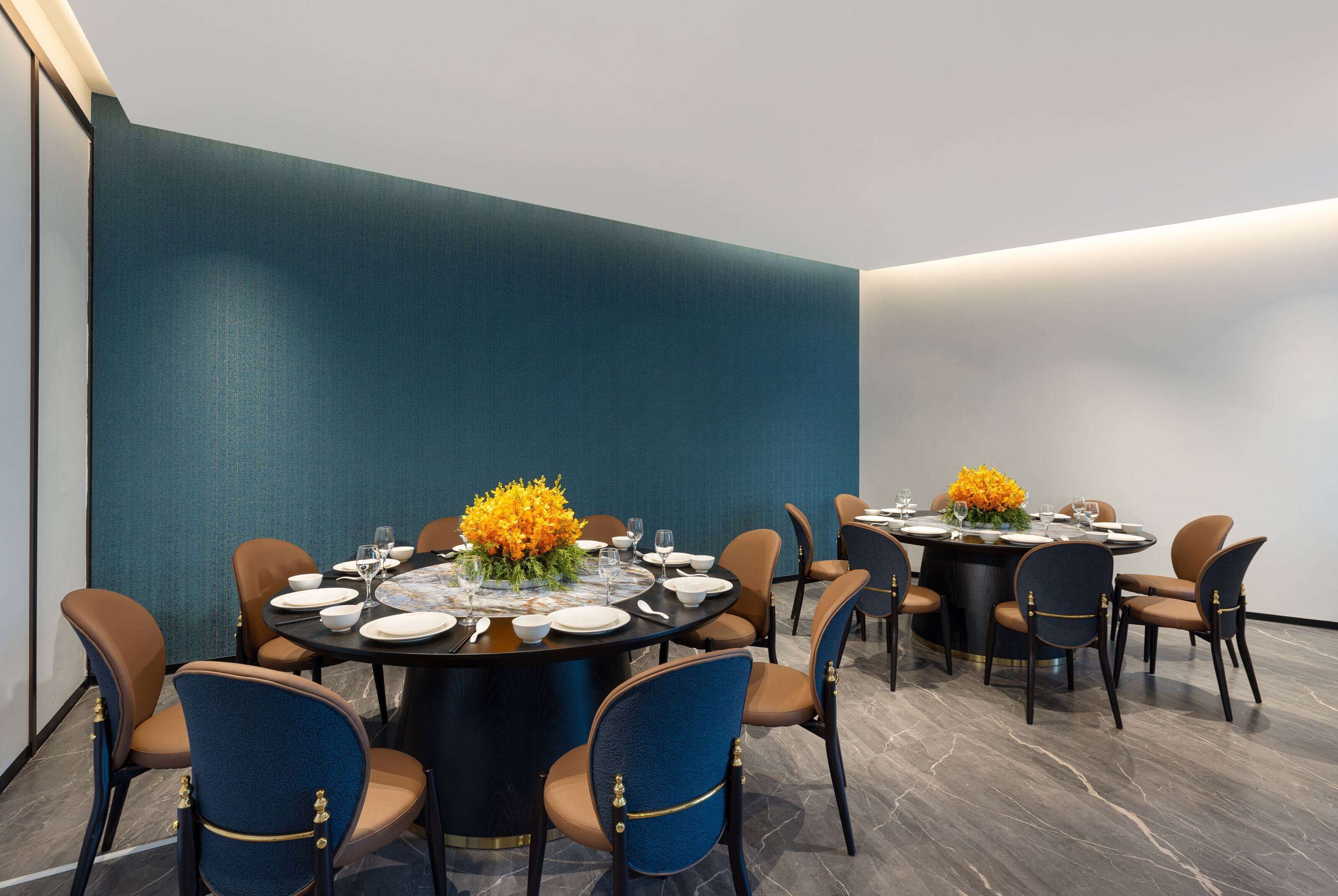 A modern dining area with round tables, blue upholstered chairs, and orange cushions.