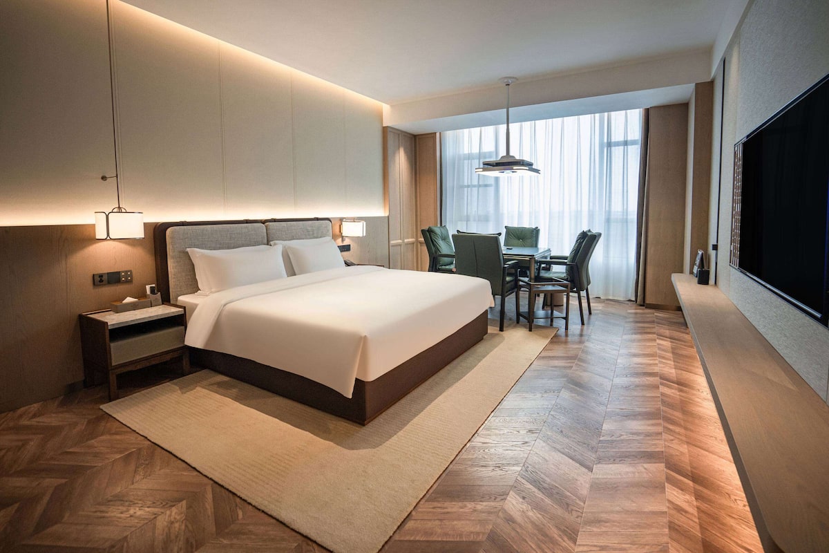 Une chambre d’hôtel moderne, dotée d’un grand lit, de tables de chevet, d’un bureau avec des chaises et d’un grand téléviseur fixé au mur.