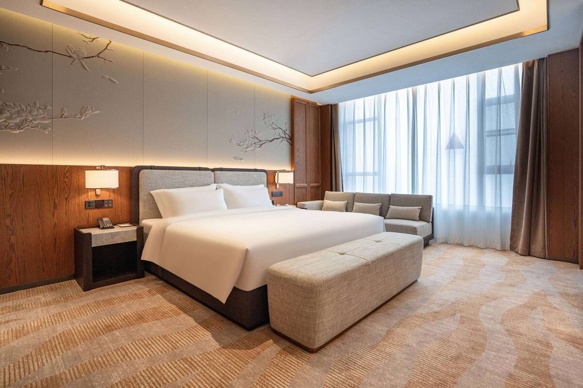 Une chambre d’hôtel moderne dotée d’un grand lit, d’un coin salon et offrant une vue sur l’extérieur par la fenêtre.
