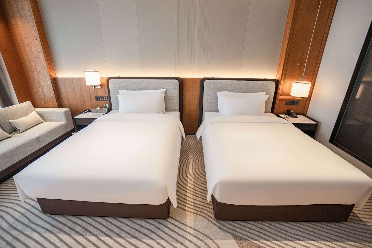 Une chambre d’hôtel avec deux lits simples, un canapé et une table de chevet avec une lampe.