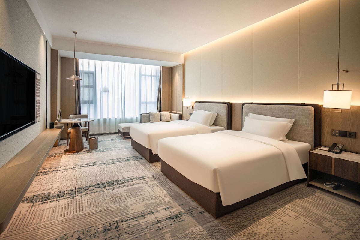 Une chambre d’hôtel avec deux lits, une télévision, un bureau et une grande fenêtre avec des rideaux.