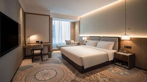 Ein Hotelzimmer mit einem großen Bett, einem Schreibtisch mit Stuhl, einem Fernseher und einem Nachttisch mit Lampe.