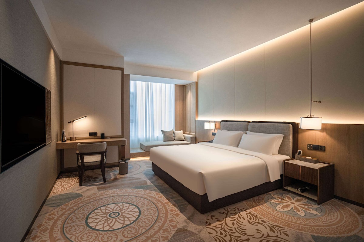 Une chambre d’hôtel avec un grand lit, un bureau avec une chaise, une télévision et une table de chevet avec une lampe.