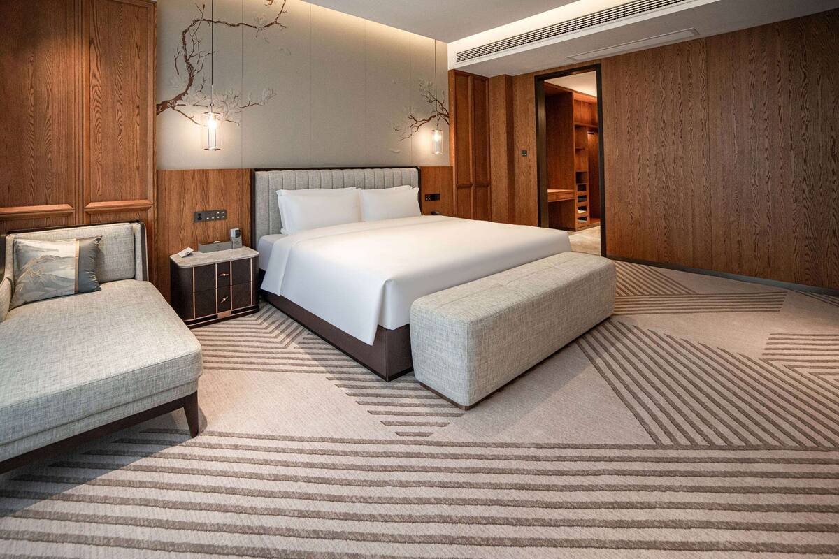 Une chambre d’hôtel moderne avec un grand lit, une banquette, une table de chevet et une armoire.