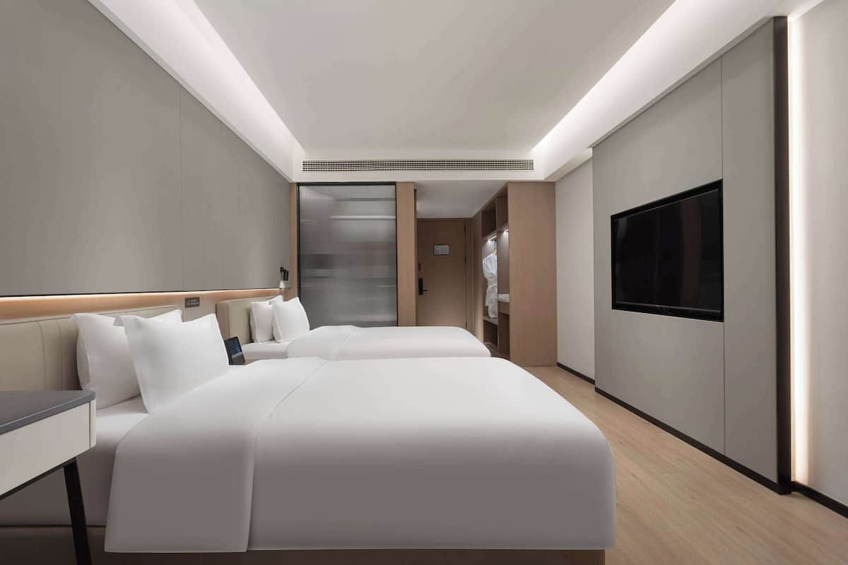 A modern hotel room with two beds, a flat-screen TV, and a walk-in closet.