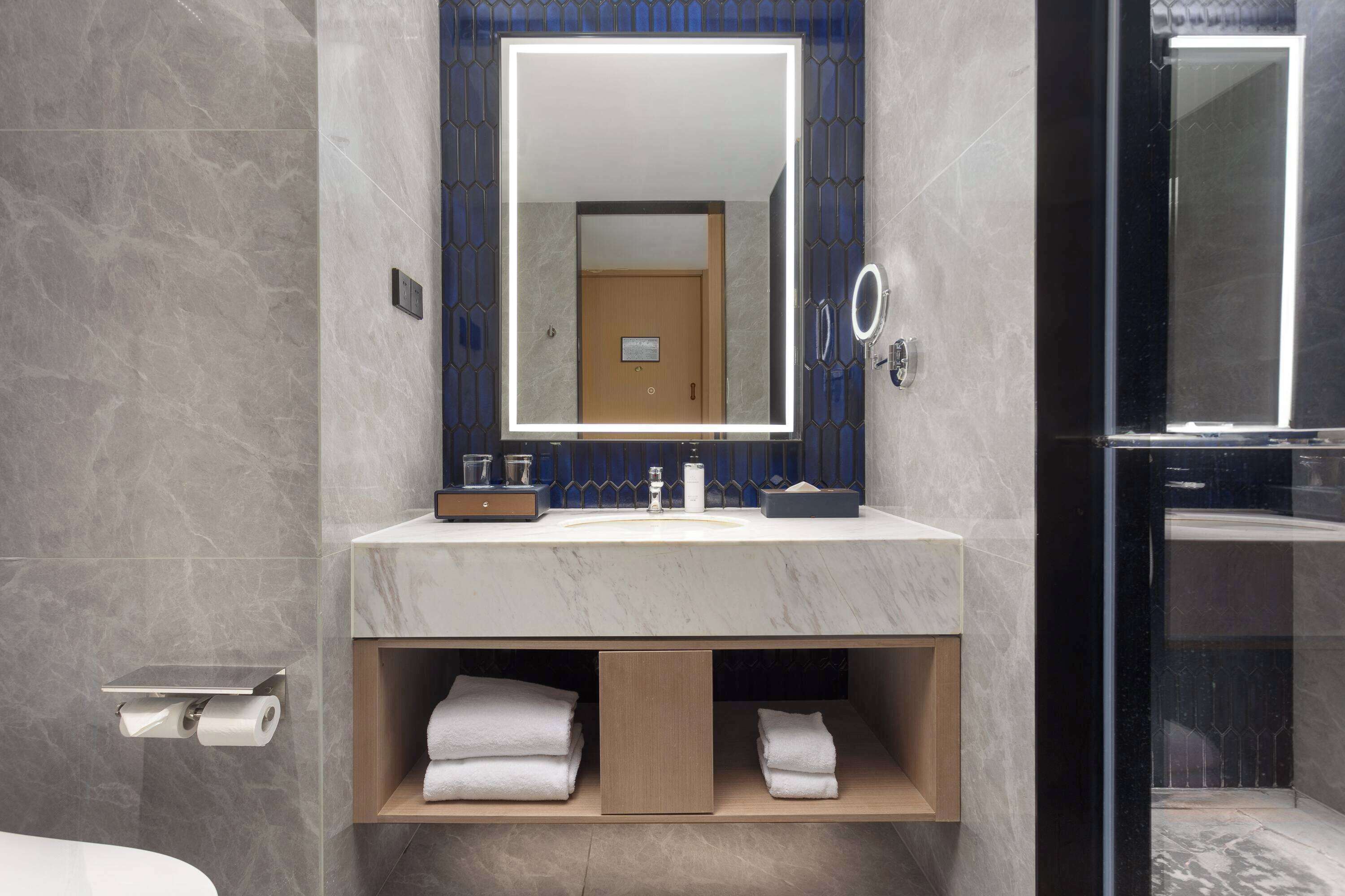 A modern bathroom with a marble sink, a large mirror, and a glass-enclosed shower.