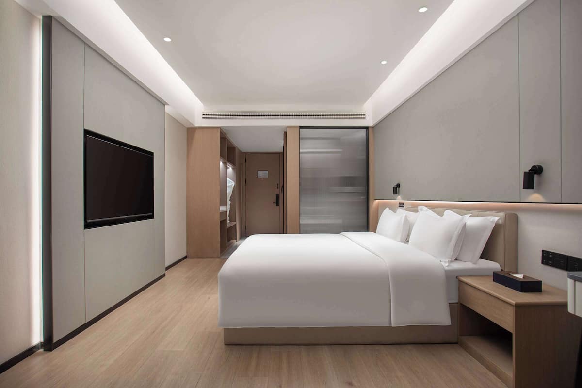 A modern hotel room with a large bed, bedside tables, a flat-screen TV, and a sliding door closet.