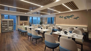 A modern conference room with wooden floors, tables, and chairs, a large screen, and a city view.