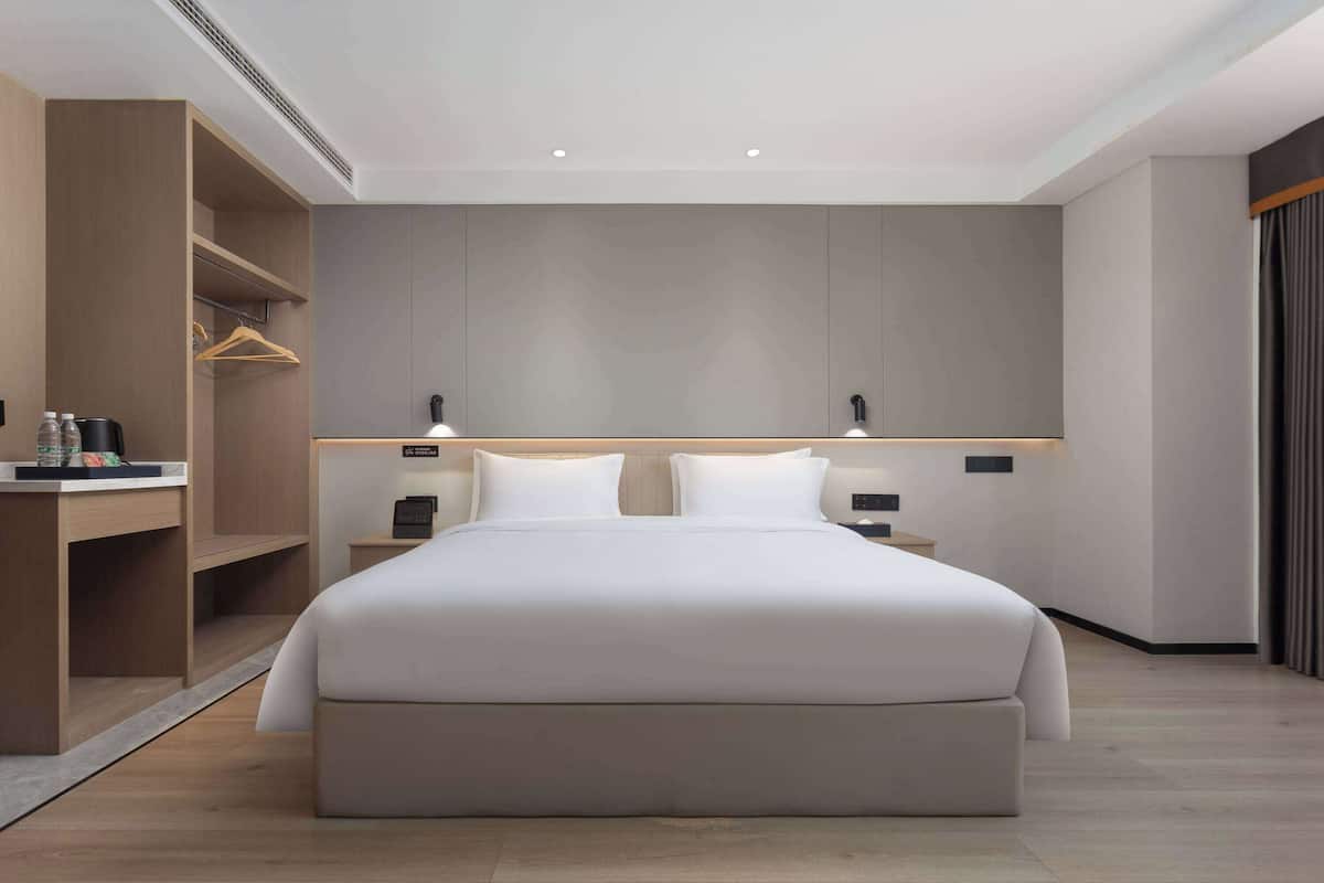 A modern hotel room with a large bed, a desk with a chair, and a wardrobe.