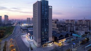 A modern hotel with a prominent glass facade, located in an urban setting with surrounding high-rise buildings.