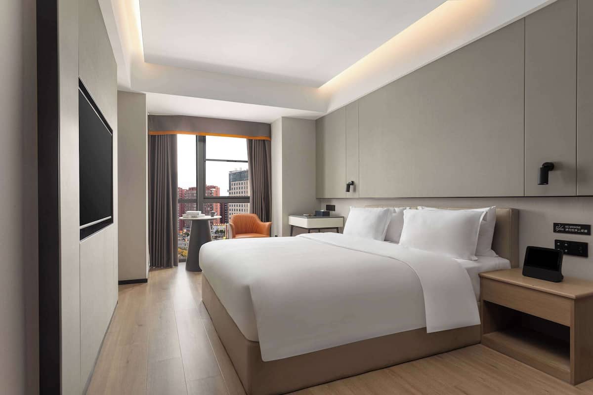A modern hotel room with a large bed, bedside tables, a TV, and a city view.