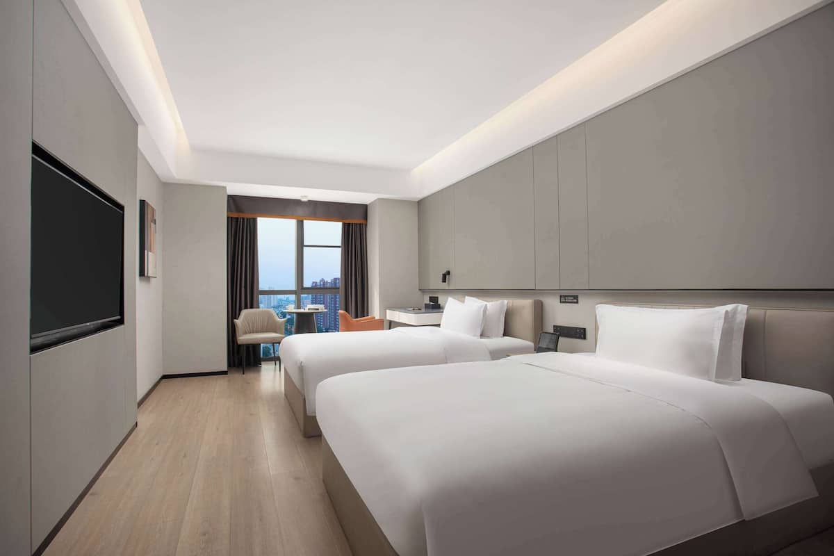 A modern hotel room with two beds, a desk, and a chair.