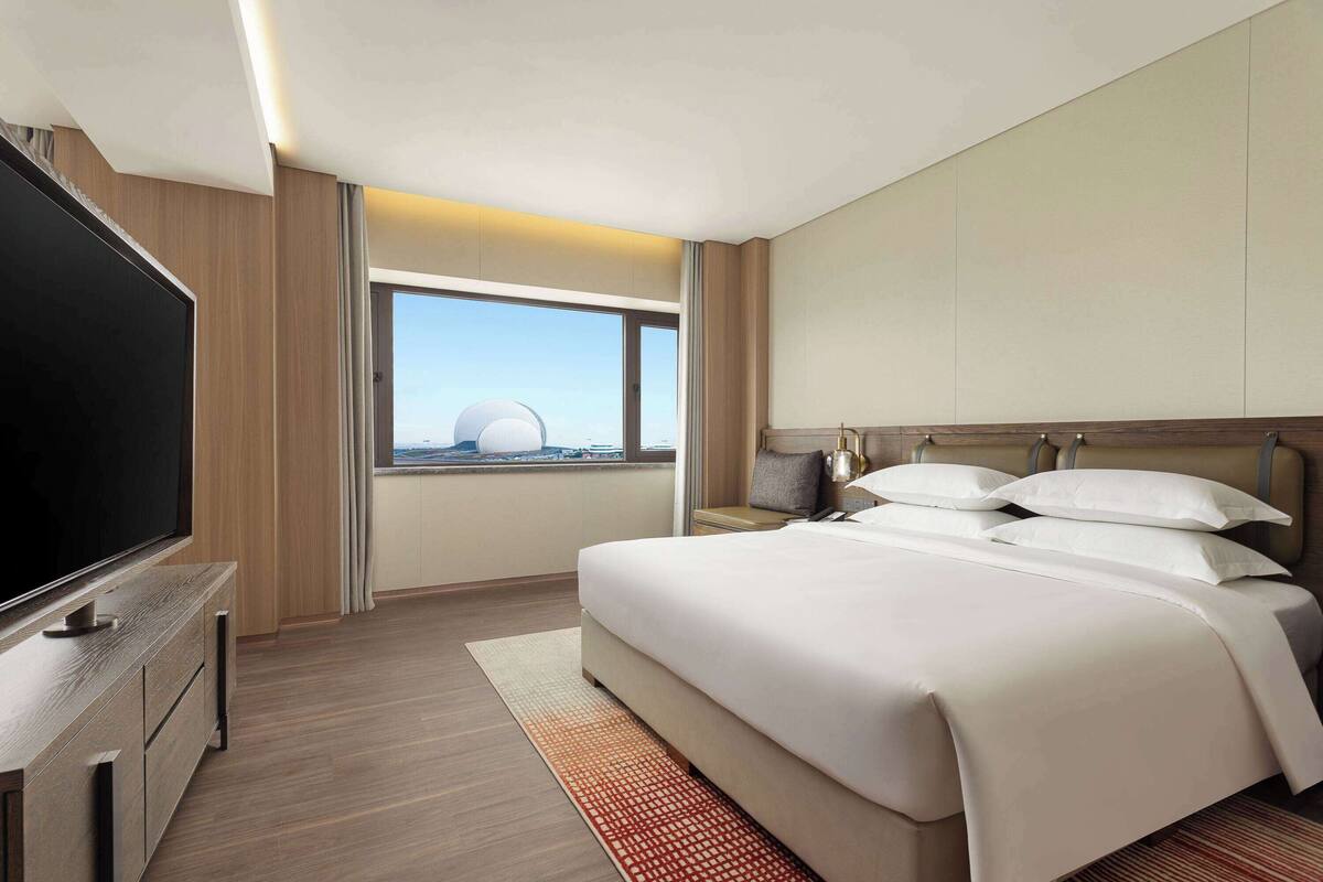 A modern hotel room with a large bed, a flat-screen TV, and a view of a dome structure.