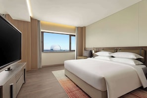 Una habitación de hotel moderna con una cama grande, un televisor de pantalla plana y vistas a una estructura en forma de cúpula.