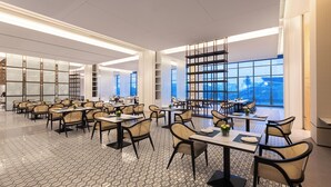Un comedor moderno con varias mesas y sillas, ventanas amplias que ofrecen vista a la ciudad y un suelo con diseño.