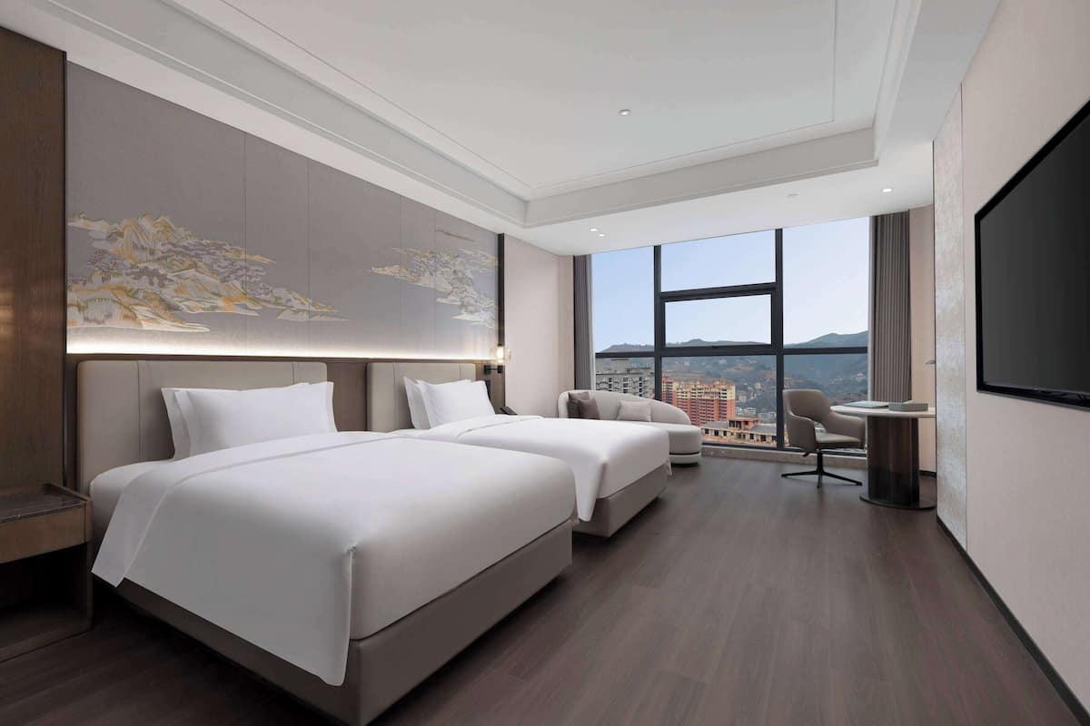 A modern hotel room with a large bed, a sofa, a desk, and a TV.